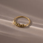 The Beaded Multiple Name Ring in 18K Gold, adorned with three custom-engraved spinning beads, is displayed on a soft, sunlit surface.