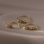 Three Beaded Multiple Name Rings in 18K Gold, each featuring small engraved beads, rest on a smooth, softly lit surface.