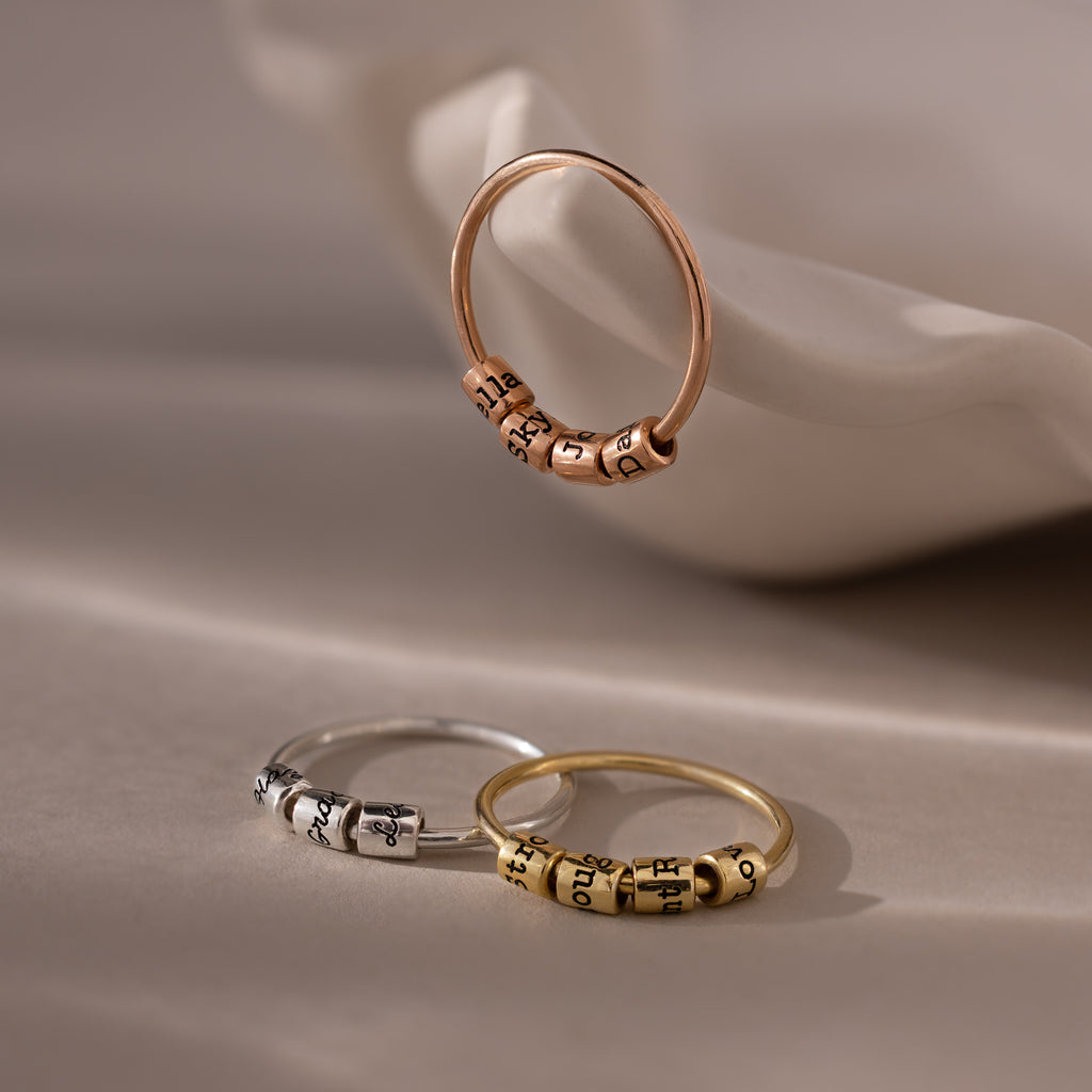 The Beaded Multiple Name Ring in Sterling Silver, engraved with names, is elegantly displayed on a white ceramic dish.