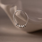 The Beaded Multiple Name Ring in Sterling Silver, engraved with "peace," rests on a soft, curved white surface.