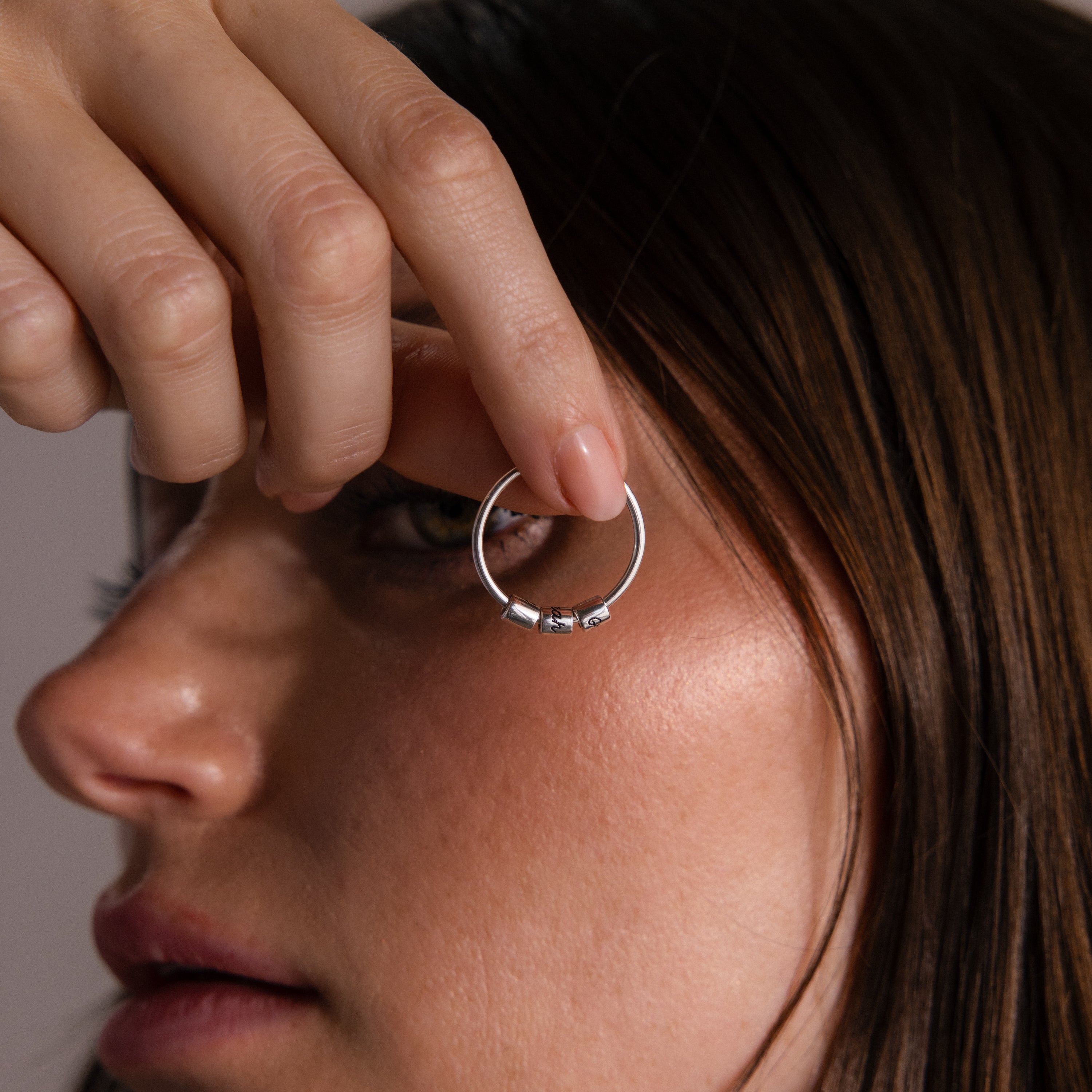 A woman holds the Beaded Multiple Name Ring in Sterling Silver near her eye, shown in a close-up side profile.