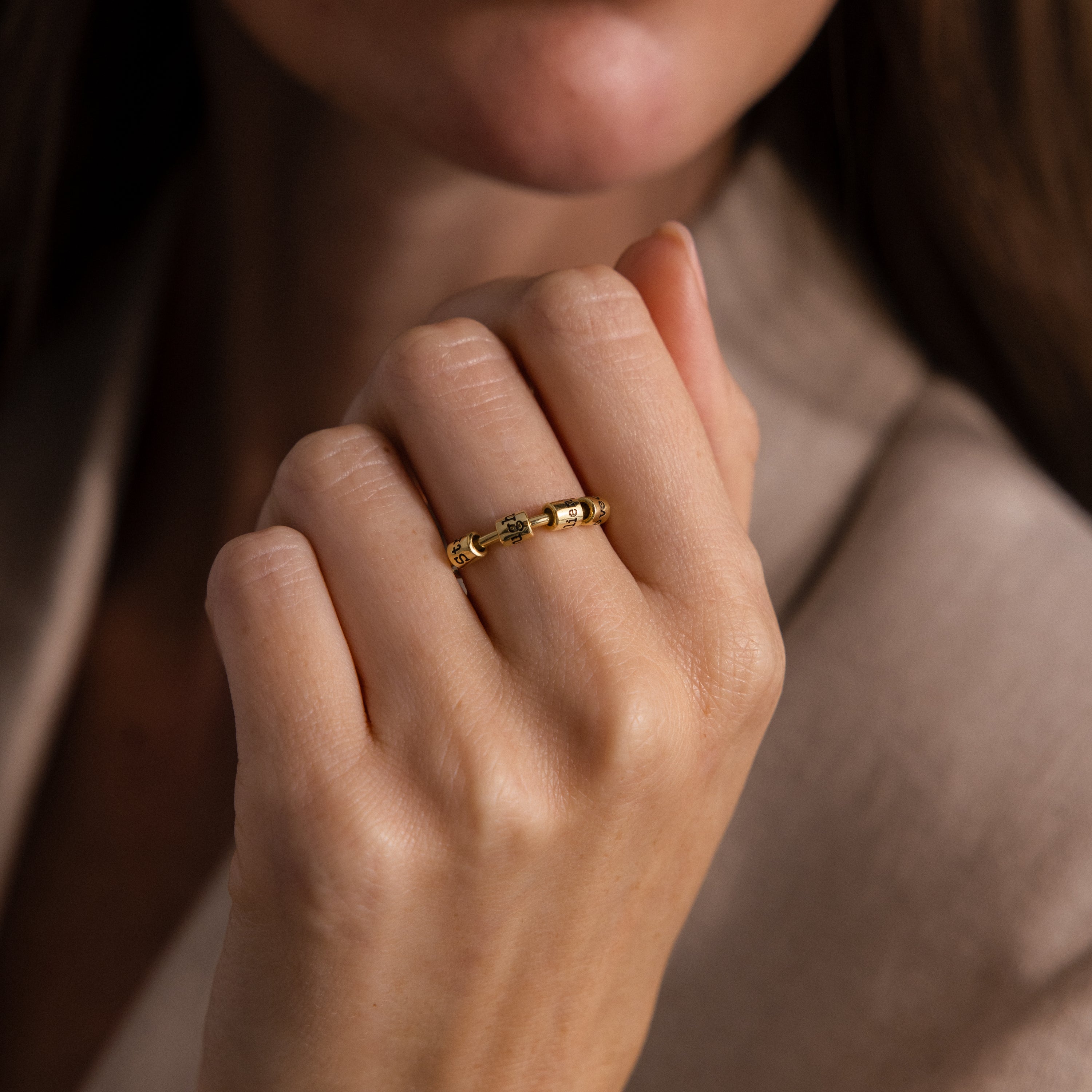 A woman's hand wearing the Beaded Multiple Name Ring in 18K Gold touches her chin, perfectly complementing her beige outfit.