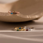 The Toi et Moi Baguette Name Ring features stacked personalized rings with engraved names and colorful gemstone accents on a neutral background.