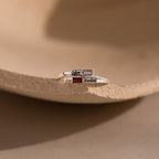 Two Toi et Moi Baguette Name Rings in Sterling Silver, personalized with engraved names Chloe and Sarah plus colorful stones, rest on a beige surface—a unique customizable name ring for any occasion.