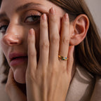A woman with brown hair touches her face, wearing a chic Toi et Moi Baguette Name Ring in 18K Gold on her finger as she looks into the camera.