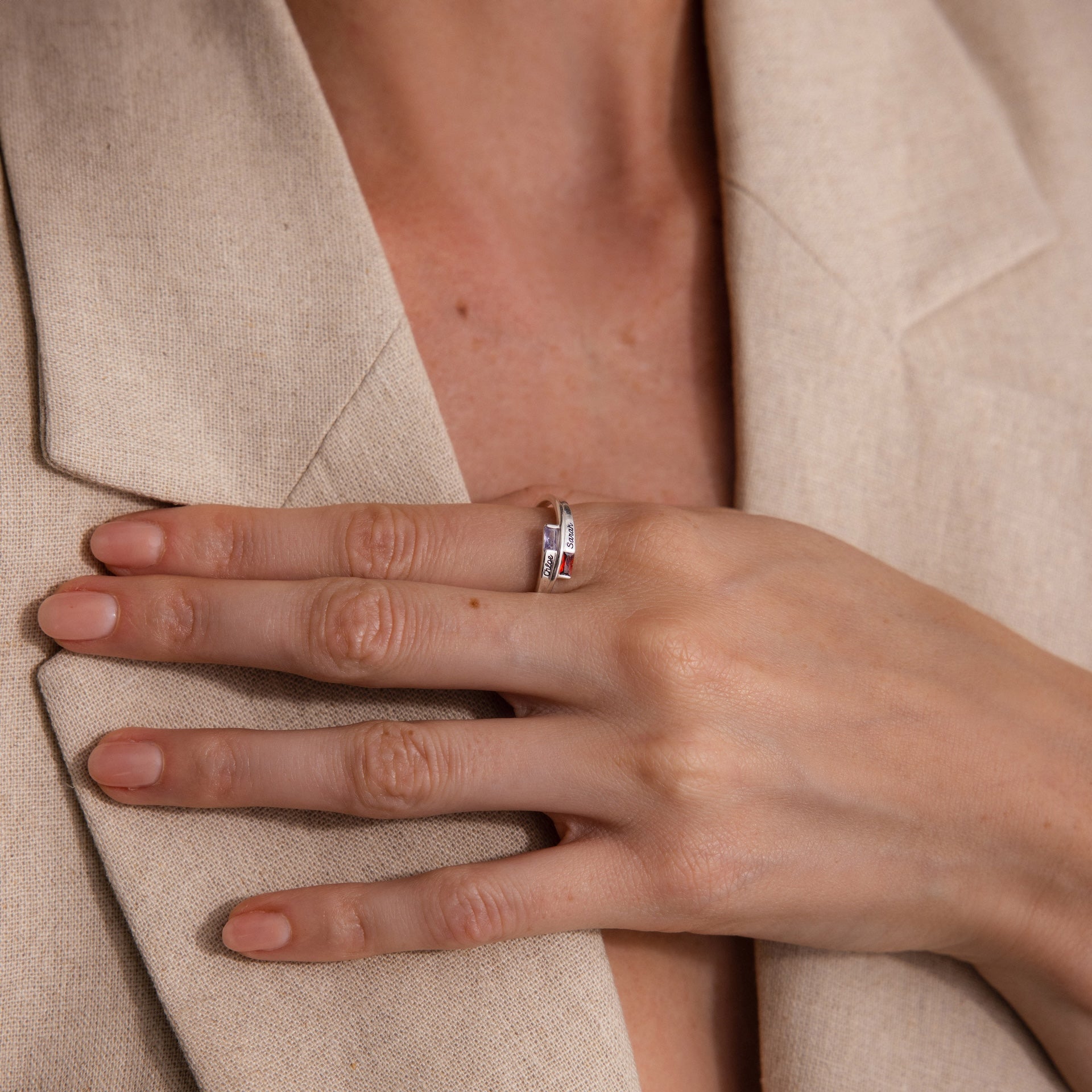A hand with neatly manicured nails wears the Toi et Moi Baguette Name Ring in Sterling Silver, resting on a beige blazer.