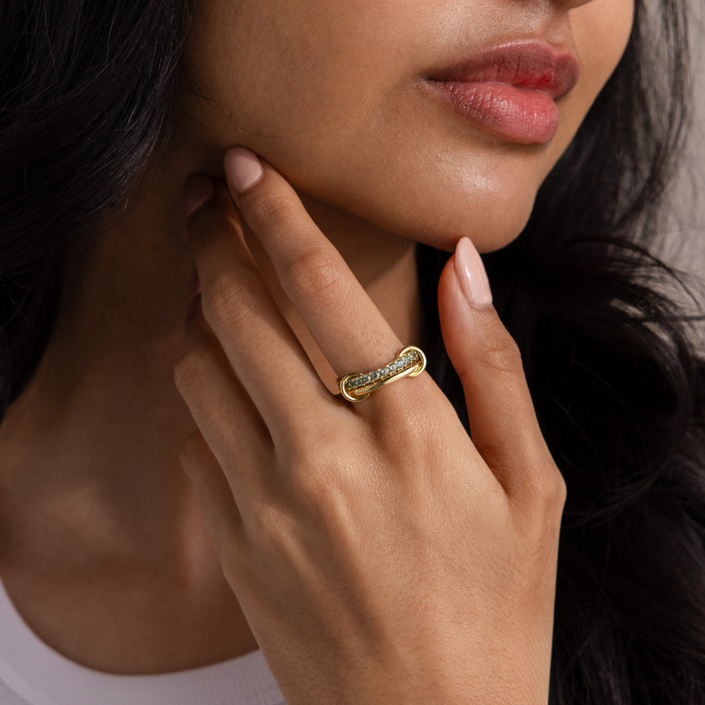 A woman touches her face, showcasing the Duo Garnet Tennis Linked Ring Set—a gold statement piece with a textured design, ideal for stacking with your favorite rings.