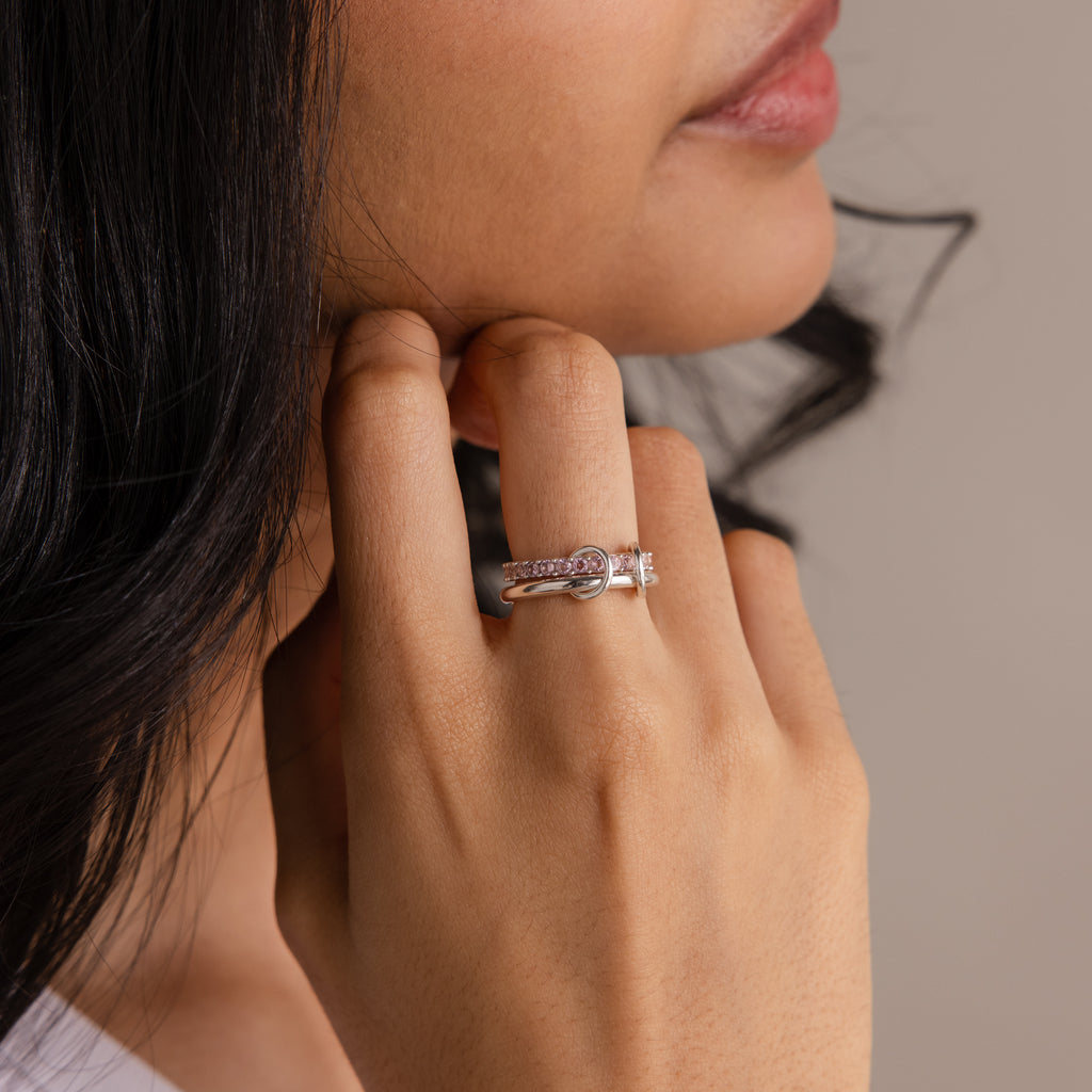 A woman's hand with the Duo Birthstone Tennis Linked Ring Set, featuring silver rings in a delicate minimalist design, rests gently on her face near her lips.