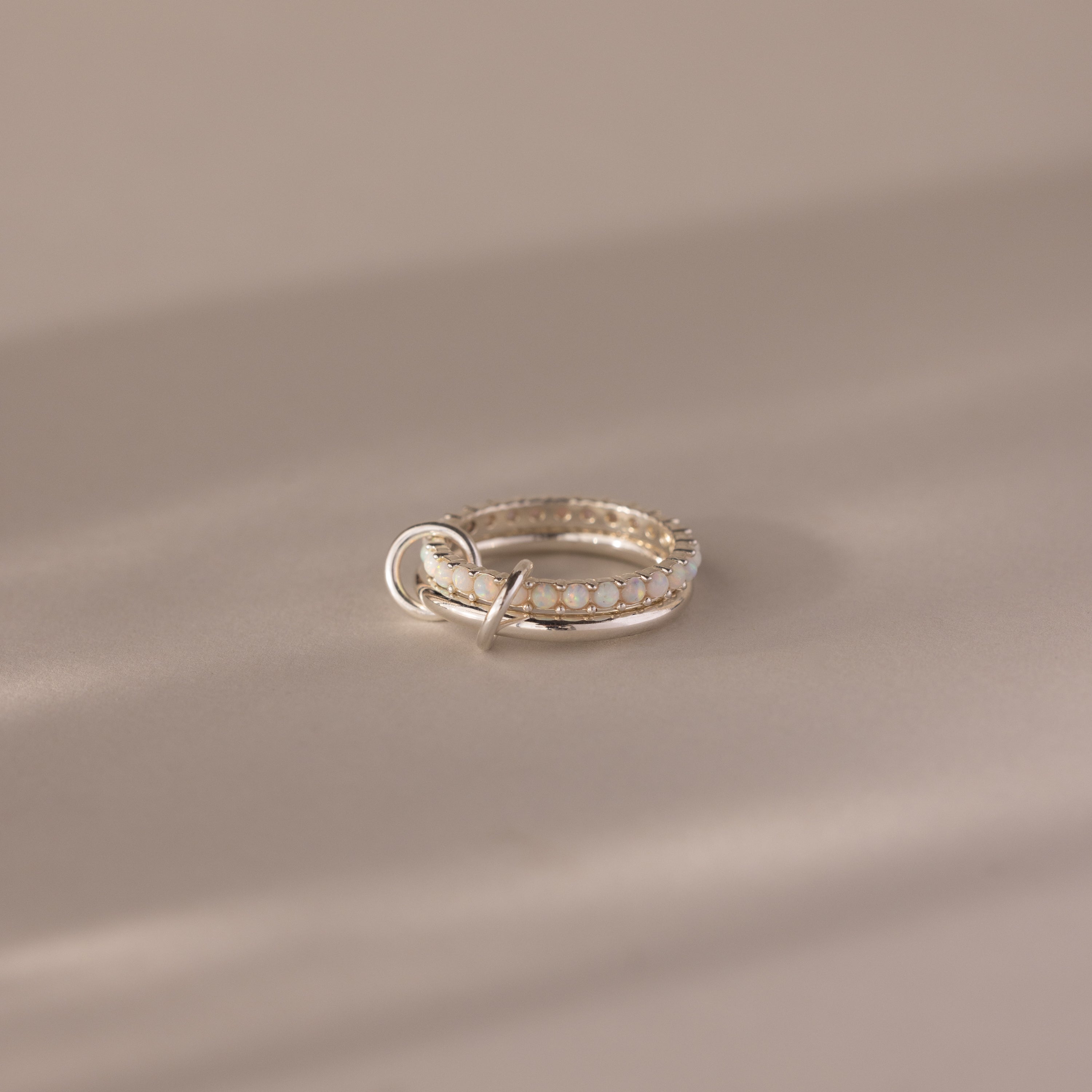 The Duo Opal Tennis Linked Ring Set rests gracefully on a smooth, beige surface.