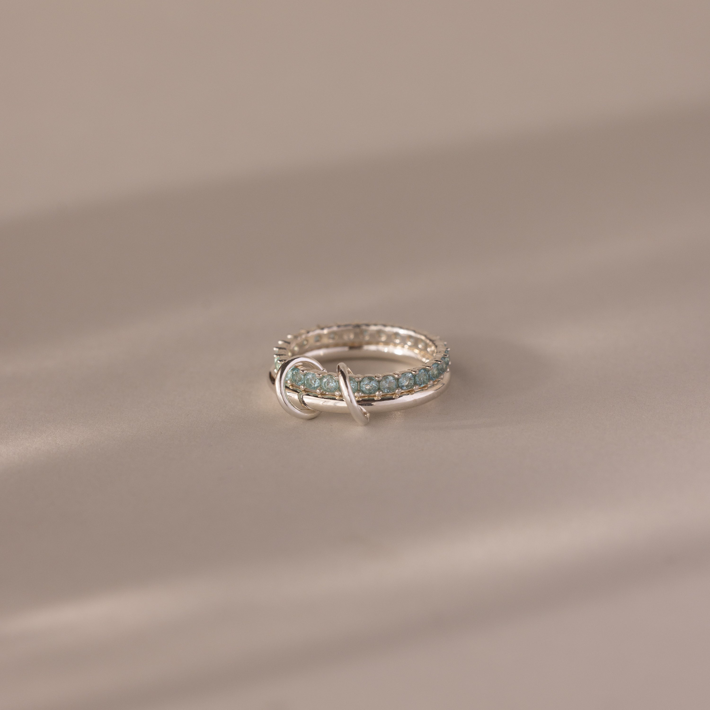 The Duo Aquamarine Tennis Linked Ring Set features light blue gemstones set in silver, shown elegantly on a soft beige surface with gentle lighting.