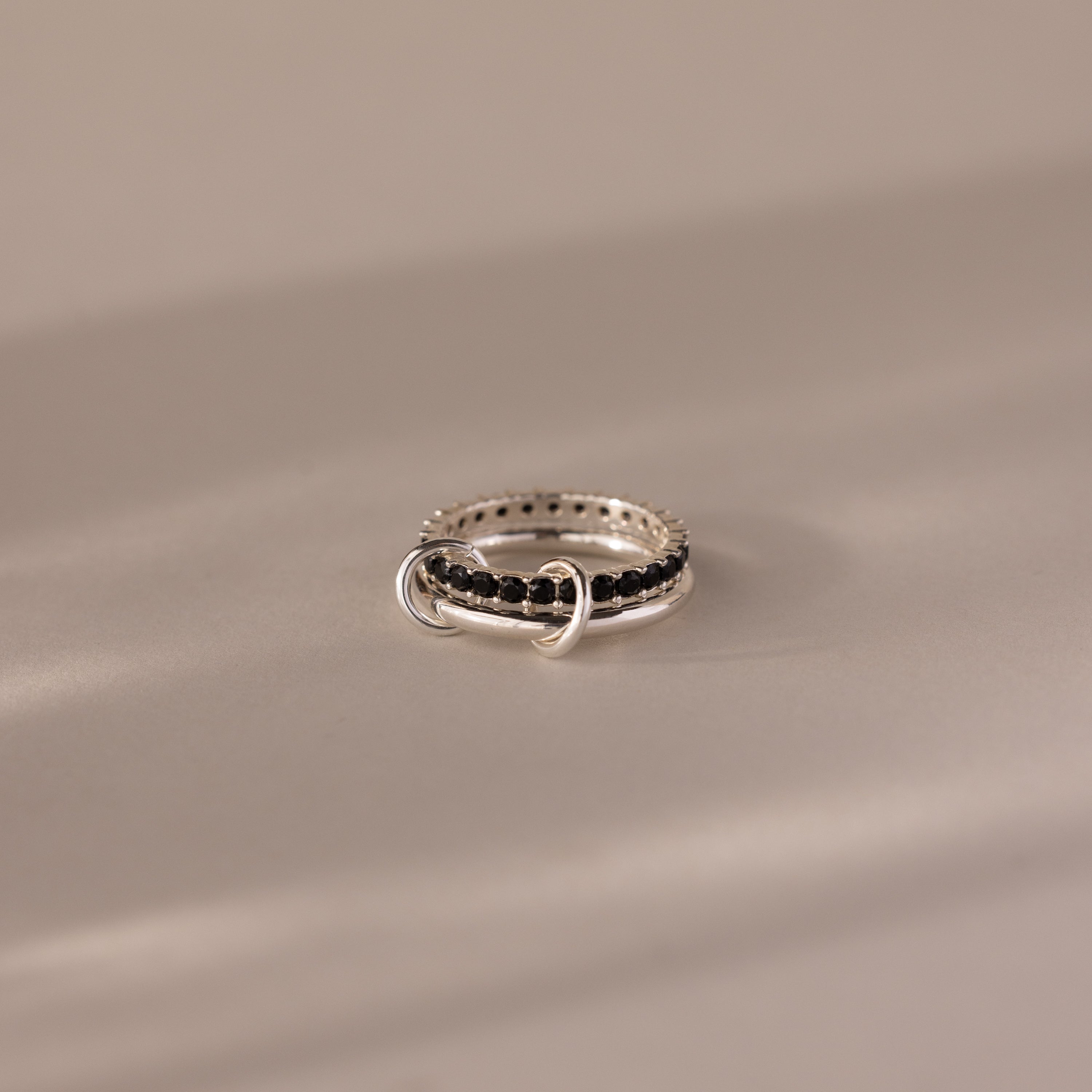 The Duo Onyx Tennis Linked Ring Set showcases minimalist black stones and two interlocking silver loops, elegantly displayed on a softly lit, neutral surface.