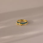 The Duo Birthstone Tennis Linked Ring Set in Blue Zircon (December) features blue gemstones set in a row on gold, displayed on a neutral, softly lit surface.