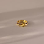 The Duo Birthstone Tennis Linked Ring Set in Garnet (January) features a minimalist, looped design with red gemstones, displayed on a soft neutral surface.