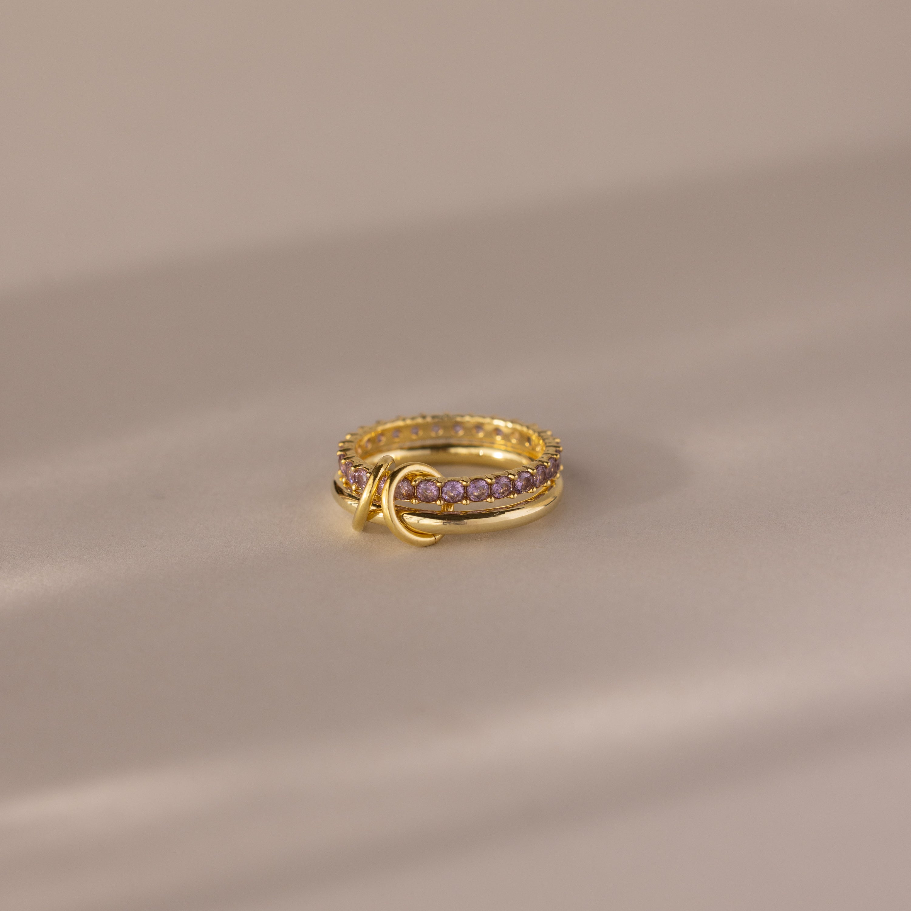 The Duo Alexandrite Tennis Linked Ring Set features small pink stones and a double loop design, elegantly displayed on a softly lit, neutral surface.