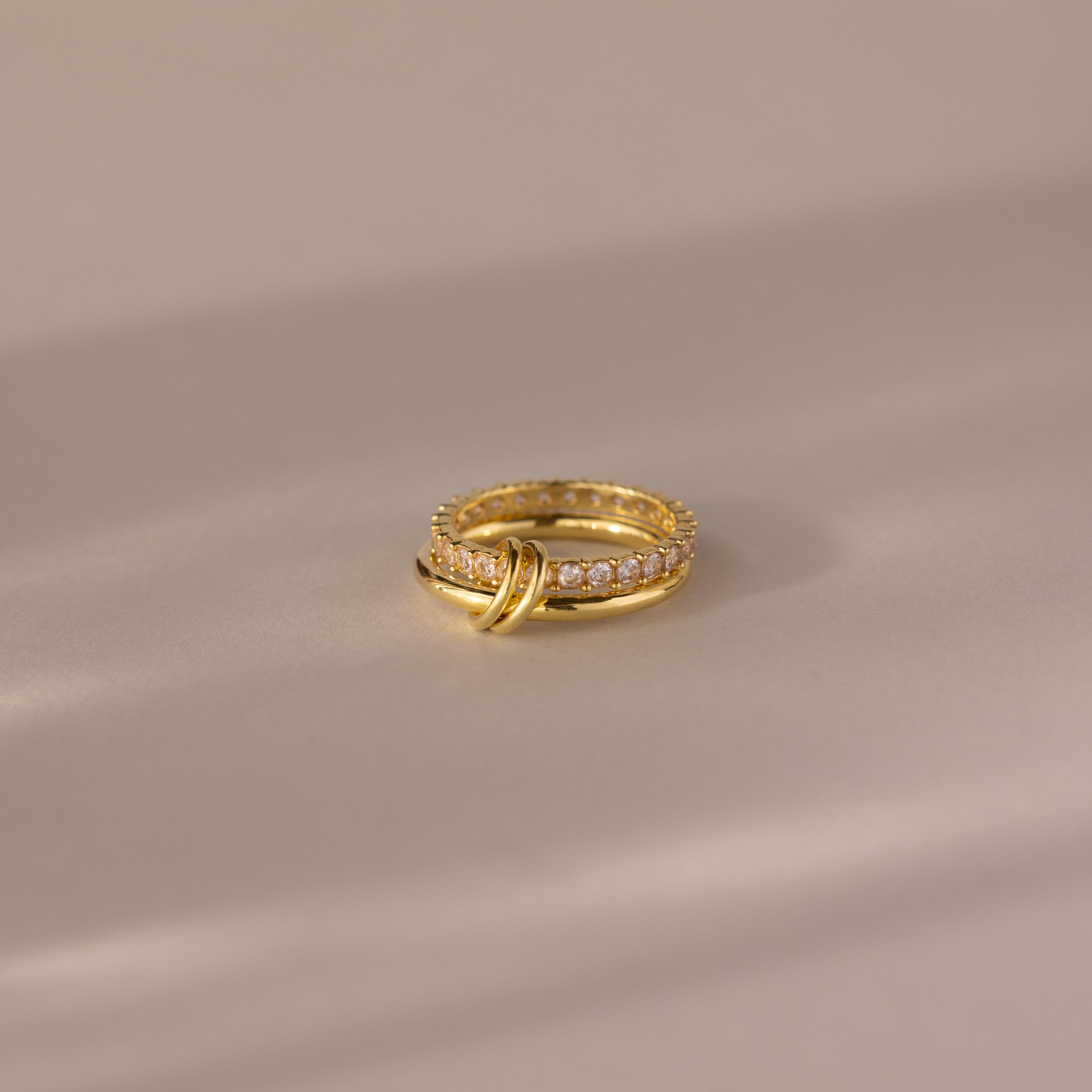 Duo Birthstone Tennis Linked Ring Set in Diamond (April) features two interlocking gold loops with small diamonds, displayed on a smooth, neutral surface.