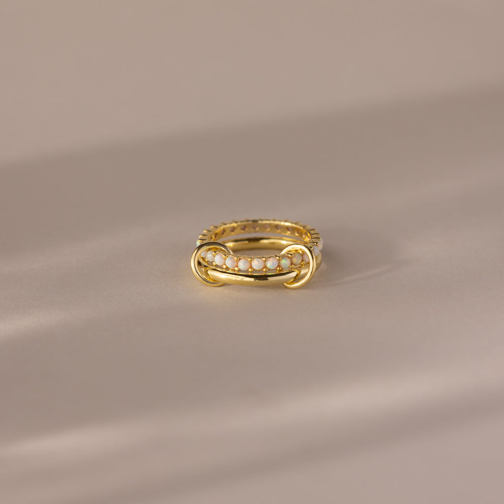 The Duo Birthstone Tennis Linked Ring Set in Opal (October) showcases minimalist linked rings with opal stones, beautifully arranged in a row and displayed on a light beige surface.