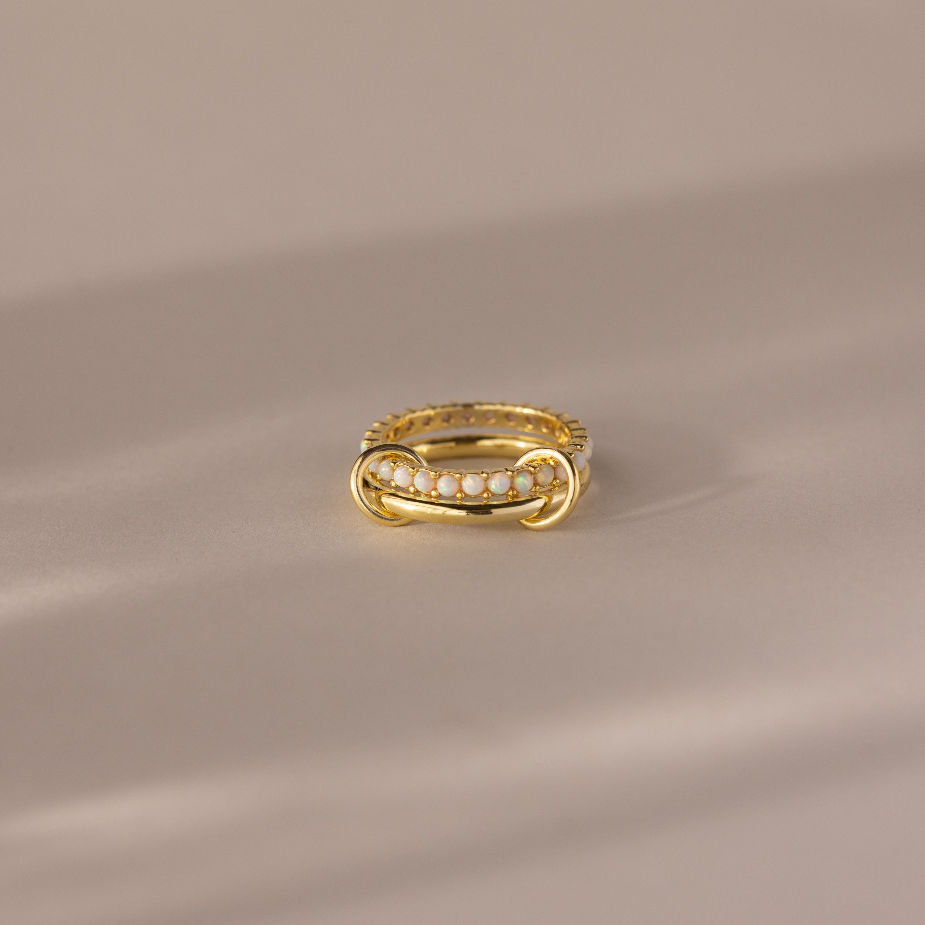 The Duo Birthstone Tennis Linked Ring Set in Opal (October) showcases minimalist linked rings with opal stones, beautifully arranged in a row and displayed on a light beige surface.