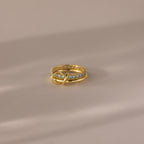 The Duo Birthstone Tennis Linked Ring Set in Aquamarine (March) features a minimalist gold band with blue stones, artfully displayed on a soft beige surface.