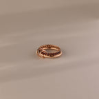 The Duo Garnet Tennis Linked Ring Set showcases small red gemstones set around the band, elegantly displayed on a beige surface.