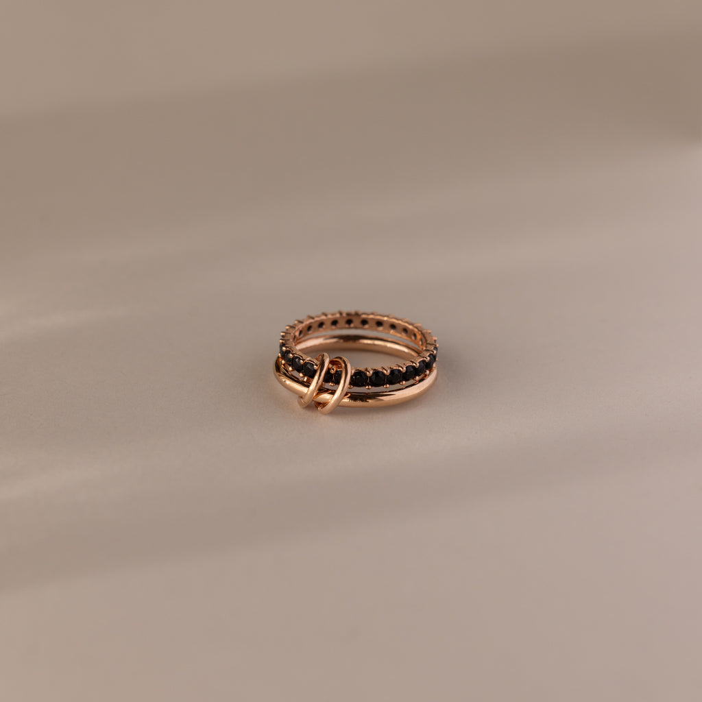 The Duo Onyx Tennis Linked Ring Set features two intertwined rings, one adorned with a textured, beaded design—an elegant pairing ideal for stacking with your favorite minimalist rings—beautifully displayed on a neutral background.