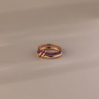 The Duo Amethyst Tennis Linked Ring Set, featuring purple amethyst gemstones and interlocking gold rings, is elegantly displayed on a beige surface.