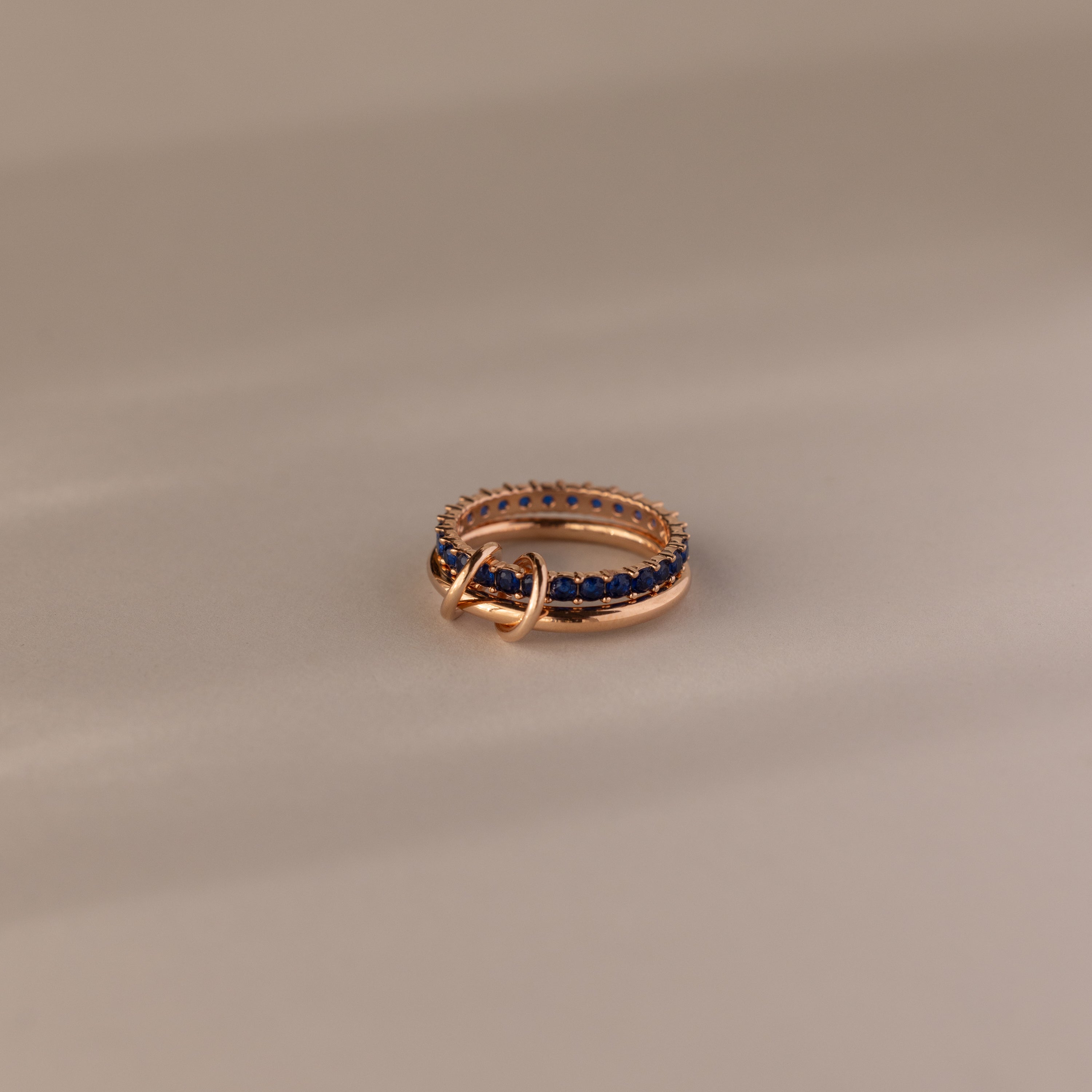The Duo Sapphire Tennis Linked Ring Set, featuring dark blue sapphires and a small connecting hoop, is displayed on a neutral background.