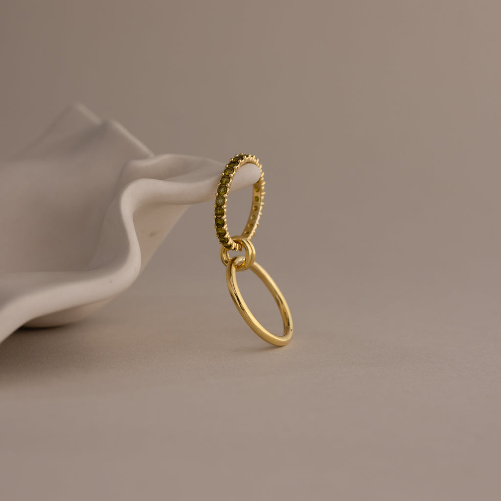The Duo Birthstone Tennis Linked Ring Set features two elegant rings—one textured, one smooth—interlinked with minimalist style, displayed gracefully on a folded white surface.