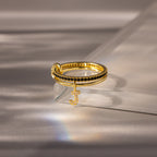 The Linked Initial Onyx Ring Set features a black stone accent and a dangling jeweled letter J charm, making it an elegant personalized jewelry piece or birthstone ring, beautifully displayed on a glass surface.