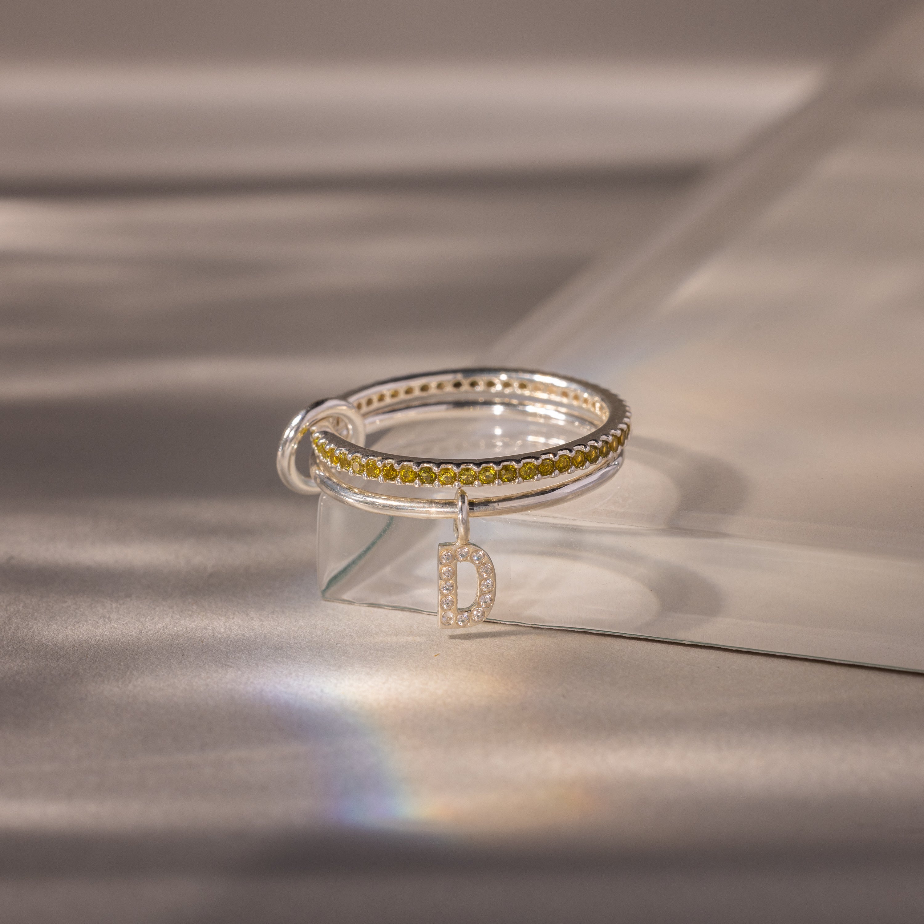 Linked Initial Peridot Ring Set featuring a yellow stone band and a dangling letter D charm, shown on a softly lit surface—an elegant birthstone piece ideal for fans of personalized jewelry.