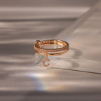 The Linked Initial Pink Tourmaline Ring Set rests on a glass surface in soft lighting, its charm sparkling elegantly.