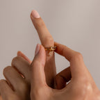 A hand slides a Linked Initial Birthstone Ring Set with a small dangling charm onto an index finger against a neutral background.