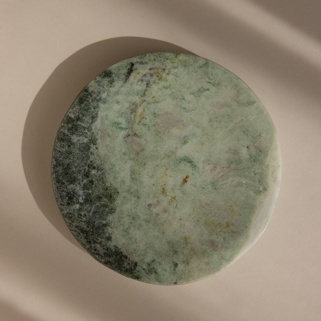 The Green Marble Jewelry Dish, featuring a round shape and greenish hues, is displayed on a beige background with soft shadows.