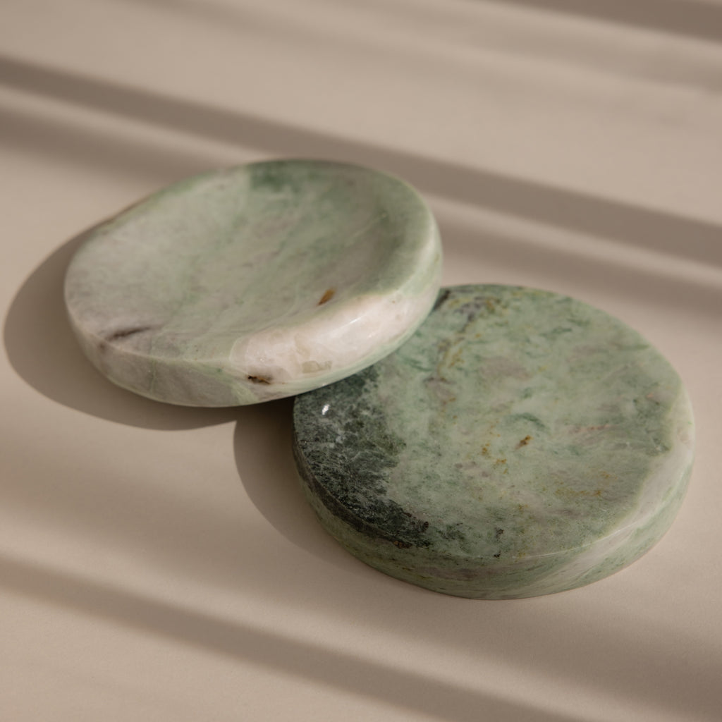 The Green Marble Jewelry Dish features a round, green marbled stone design and rests on a beige surface with soft shadows—ideal as an elegant holder for your favorite jewelry pieces.