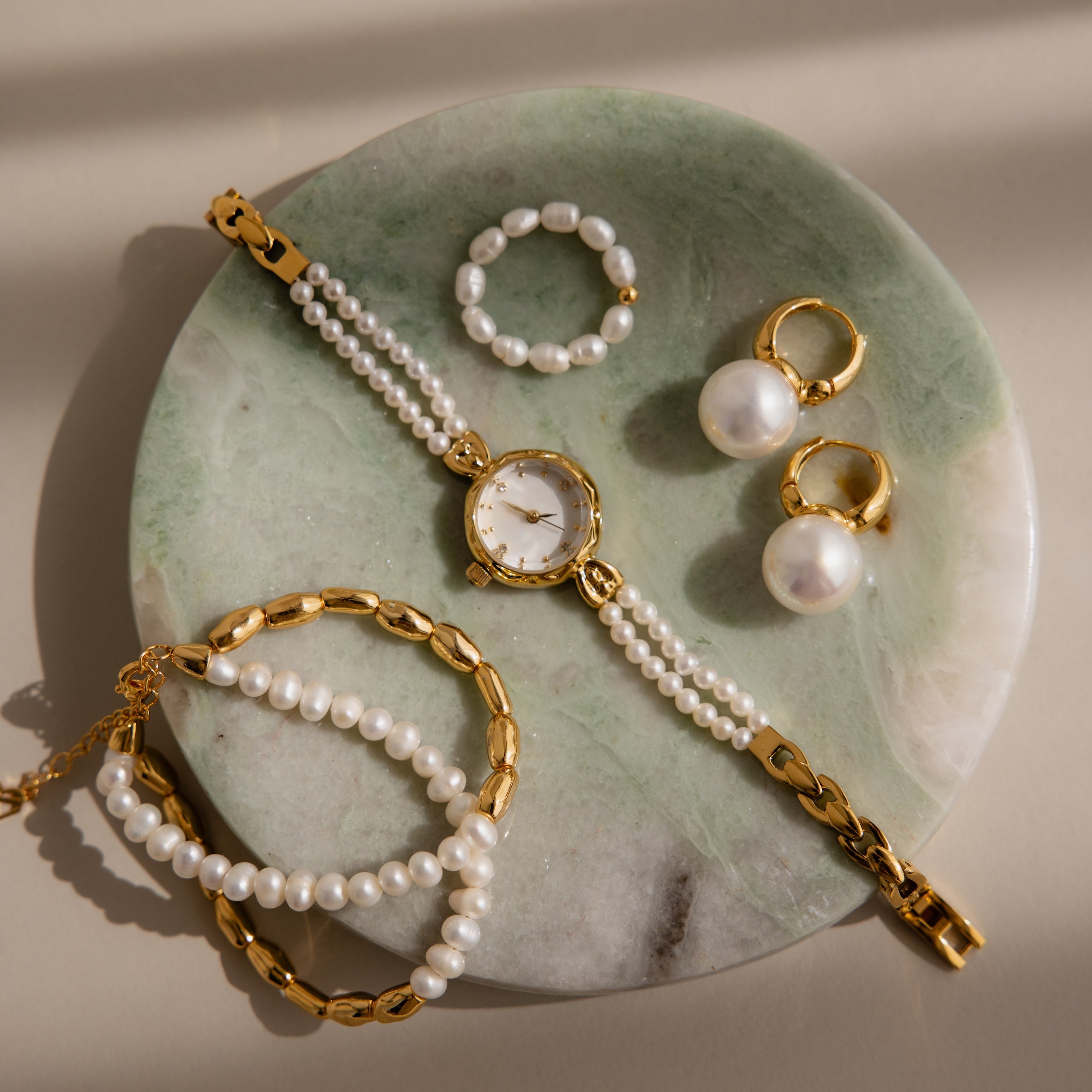 Gold and pearl jewelry—watch, rings, earrings, and bracelets—elegantly arranged on a Green Marble Jewelry Dish.