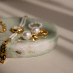 Gold and pearl jewelry pieces rest on the Marble Jewelry Dish, which is crafted from green marble and illuminated by soft natural light.