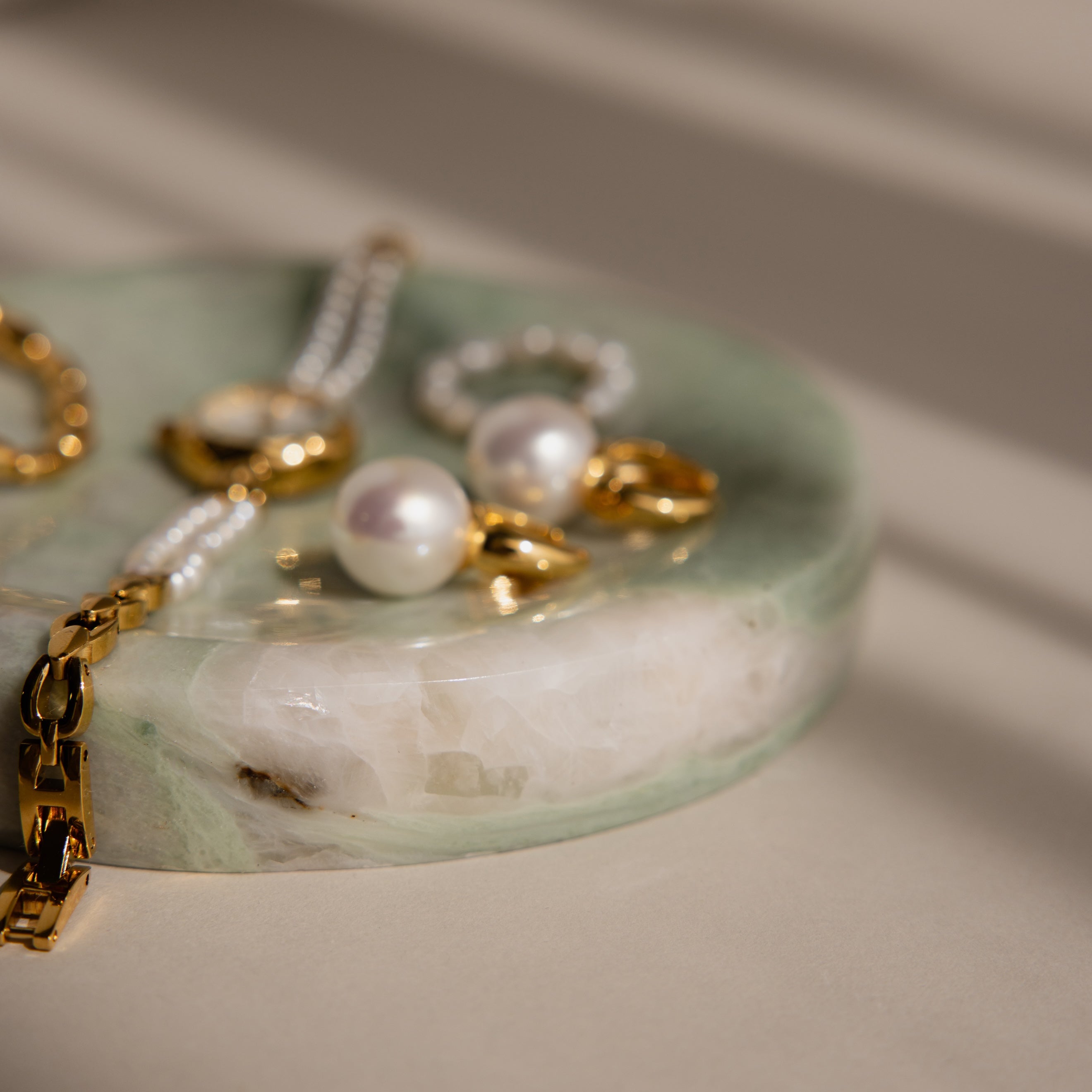 Gold and pearl jewelry pieces rest on the Marble Jewelry Dish, which is crafted from green marble and illuminated by soft natural light.