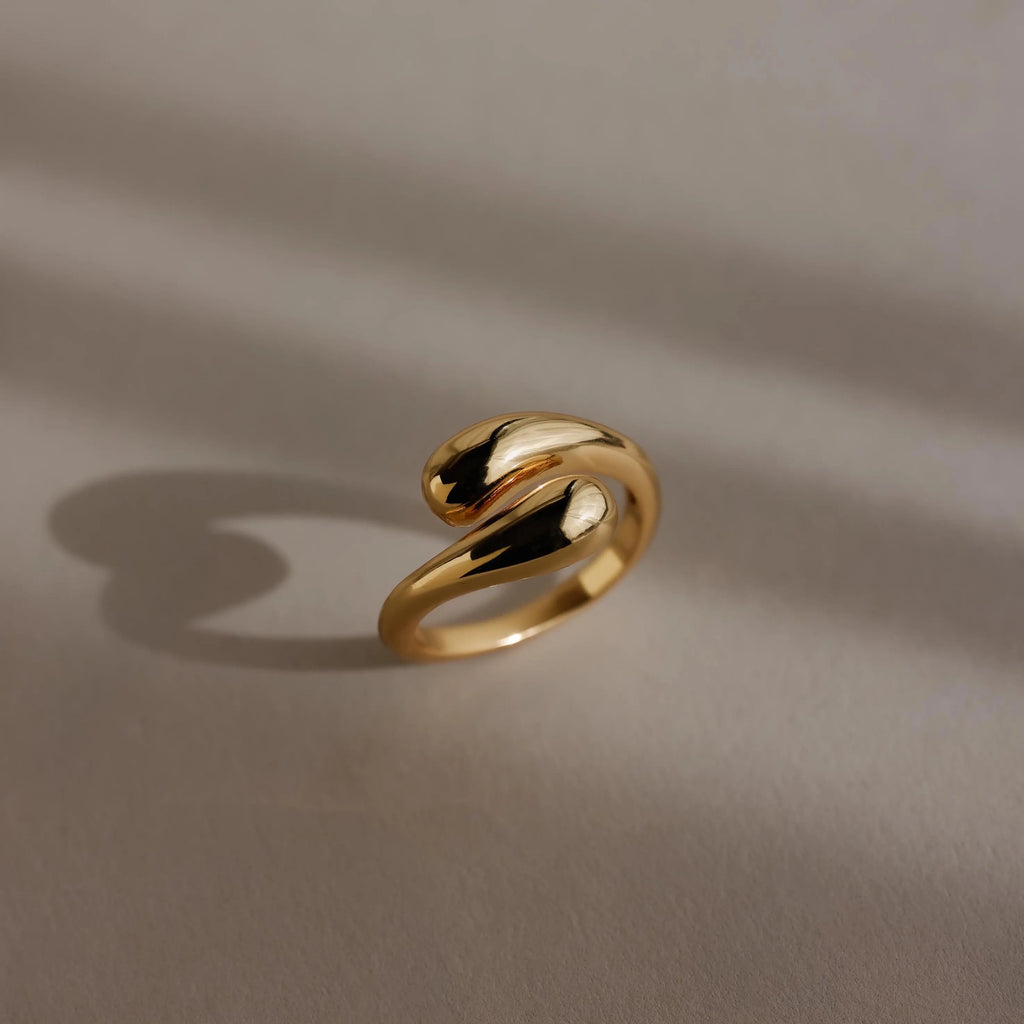 The gold Duo Dome Ring, featuring an open-ended adjustable band, rests on a neutral textured surface and casts a gentle shadow.