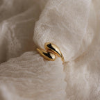A Duo Dome Ring featuring a curved, sculptural design rests on soft, textured white fabric.