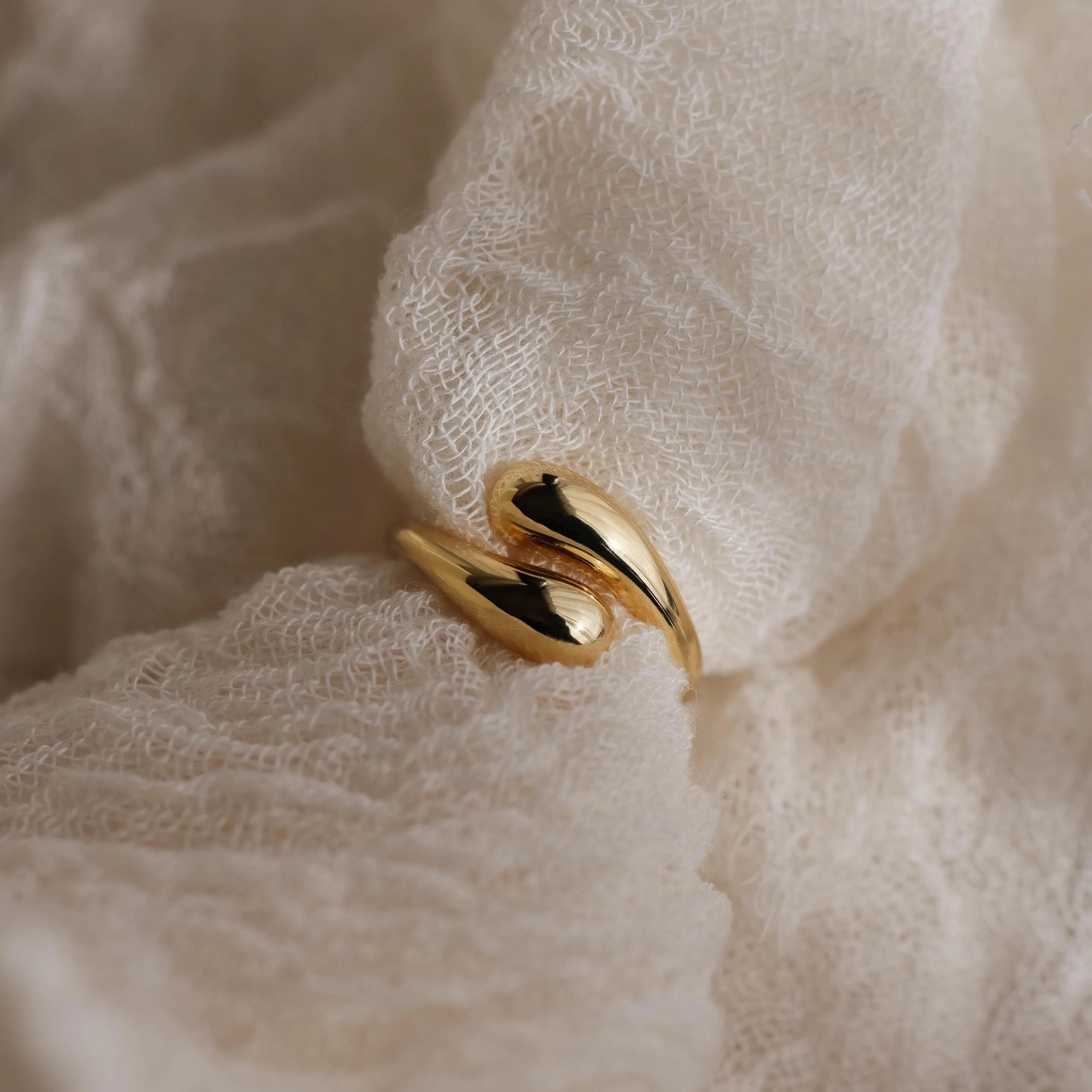 A Duo Dome Ring featuring a curved, sculptural design rests on soft, textured white fabric.