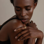 A woman with short curly hair looks down, wearing a black top and the Duo Dome Ring with an adjustable band, hand resting on her shoulder.