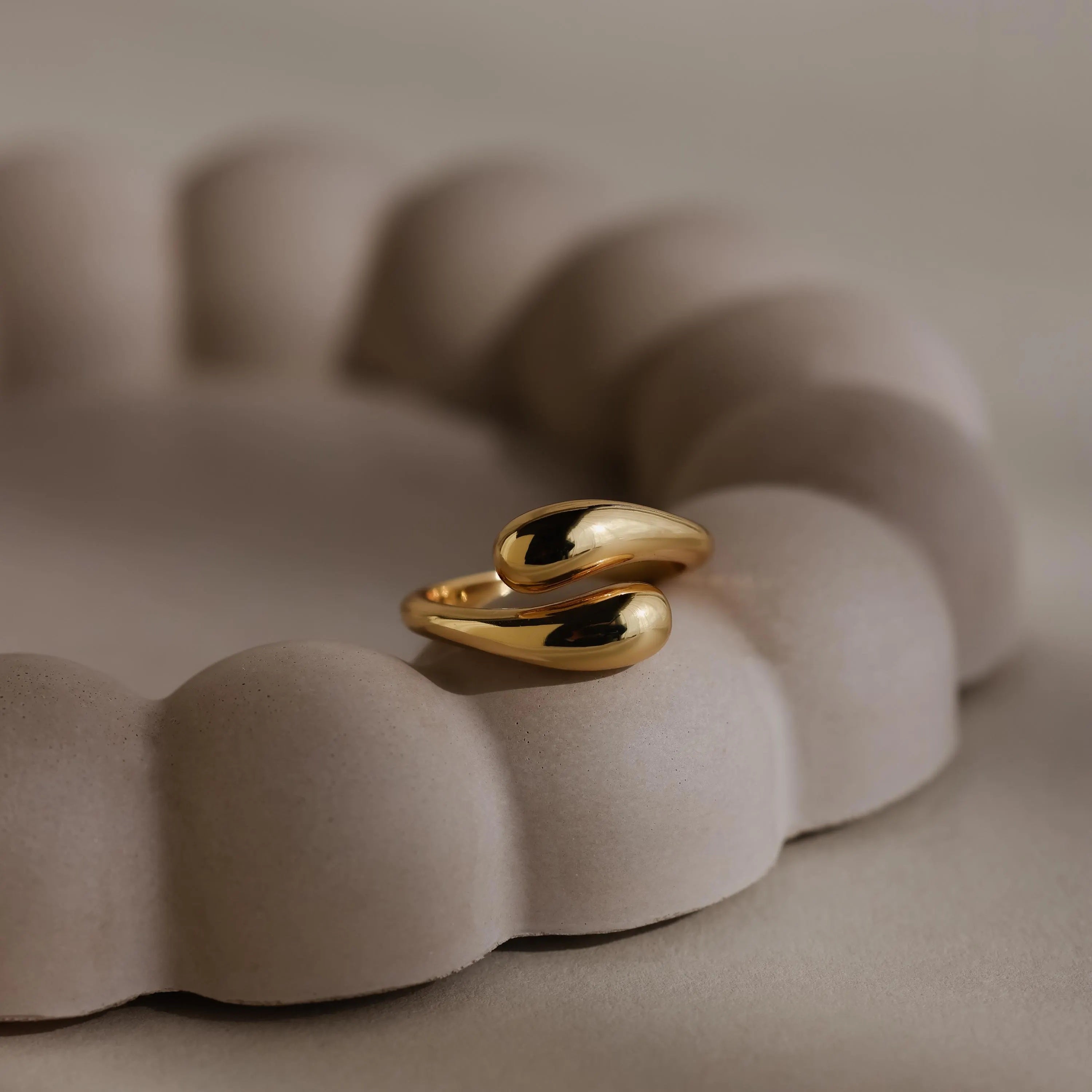 The gold Duo Dome Ring, featuring an adjustable band and sculptural design, rests on a beige scalloped ceramic holder.
