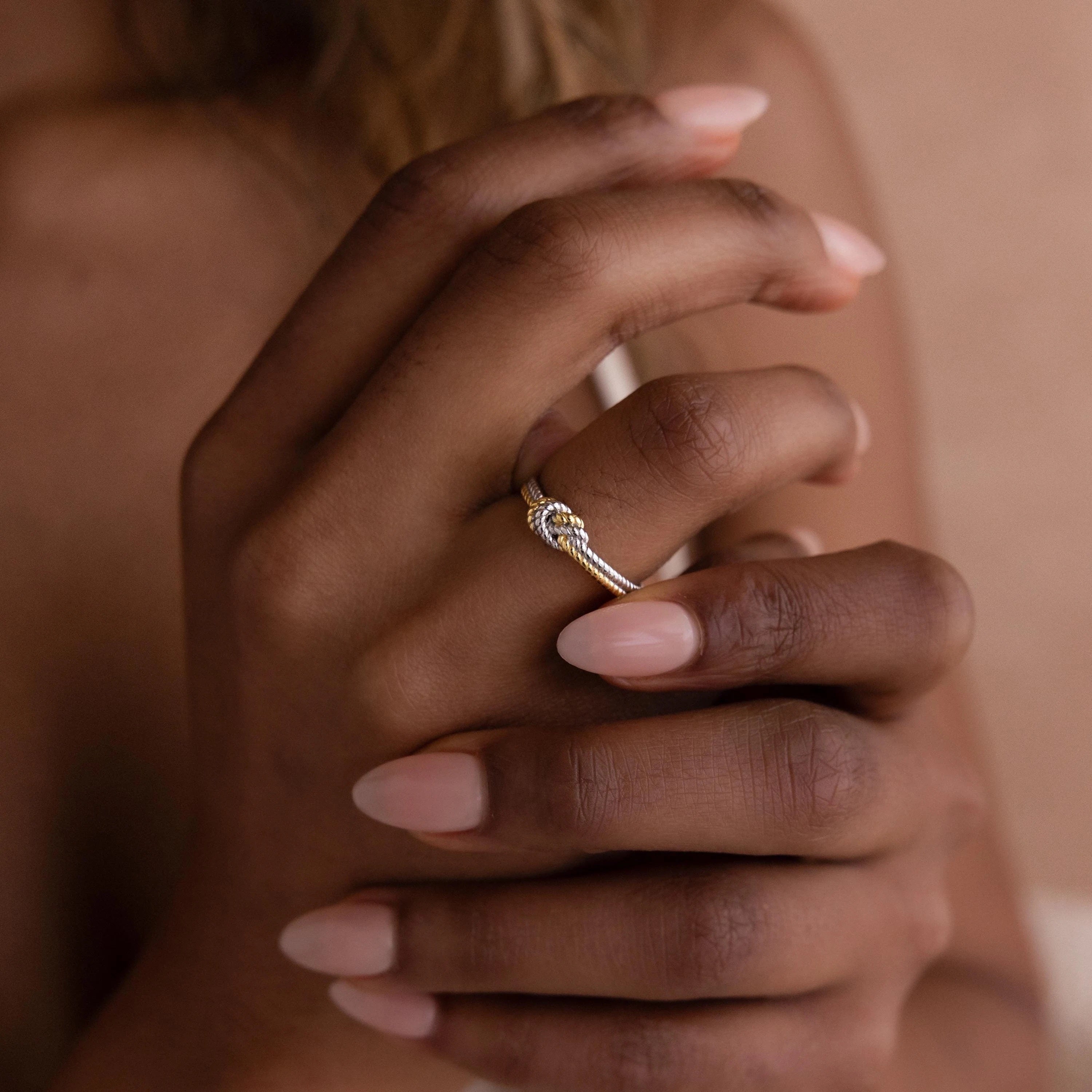 Close-up of hands with natural nails, one wearing the Mixed Metal Knot Ring—a chic gold and silver band featuring a unique knot design, making it an ideal relationship gift.