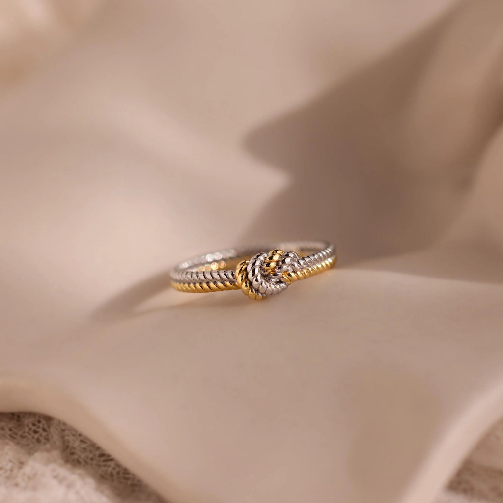 The Mixed Metal Knot Ring, expertly crafted with twisted gold and silver, is beautifully showcased on soft beige fabric—a meaningful gift that celebrates unity and connection.