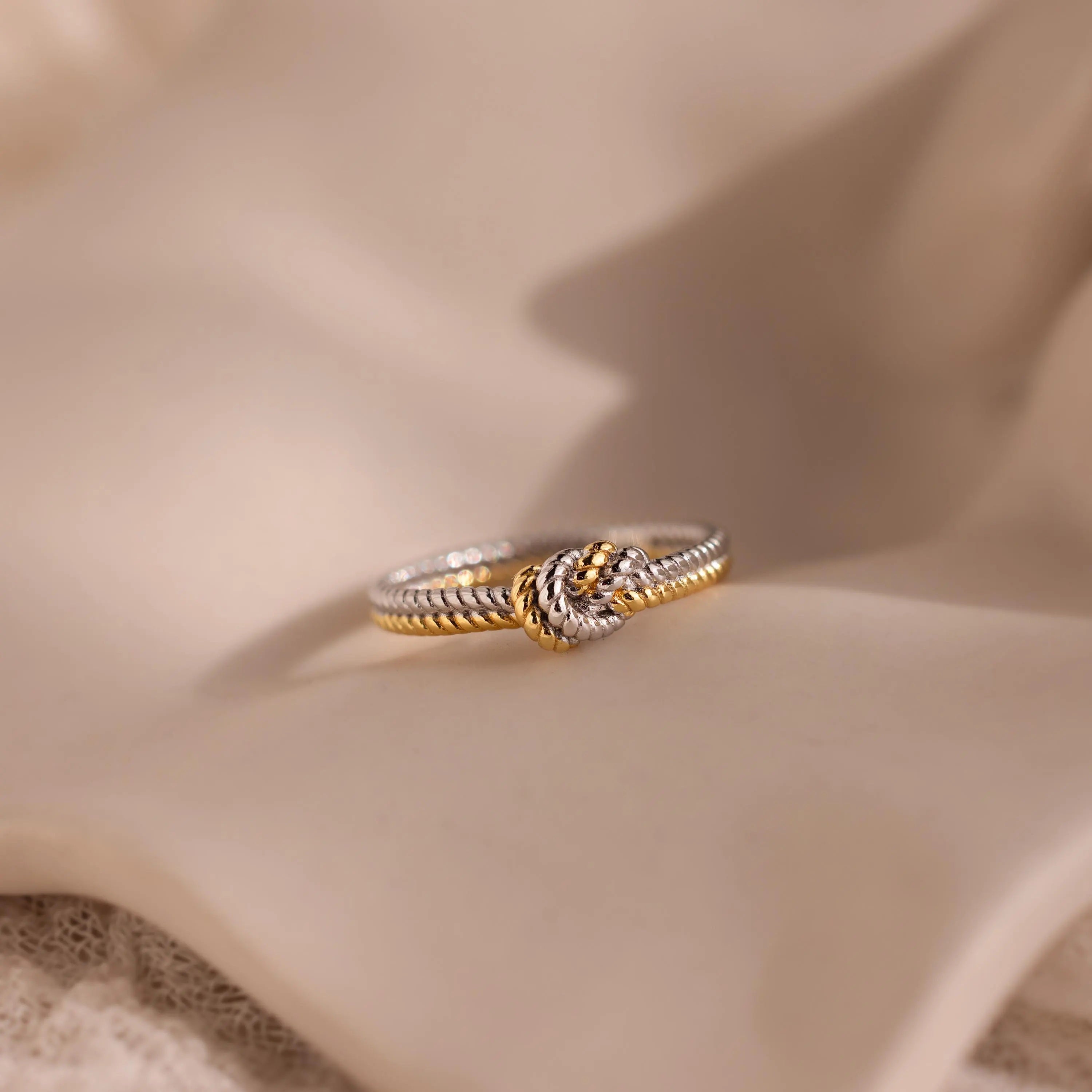 The Mixed Metal Knot Ring, expertly crafted with twisted gold and silver, is beautifully showcased on soft beige fabric—a meaningful gift that celebrates unity and connection.