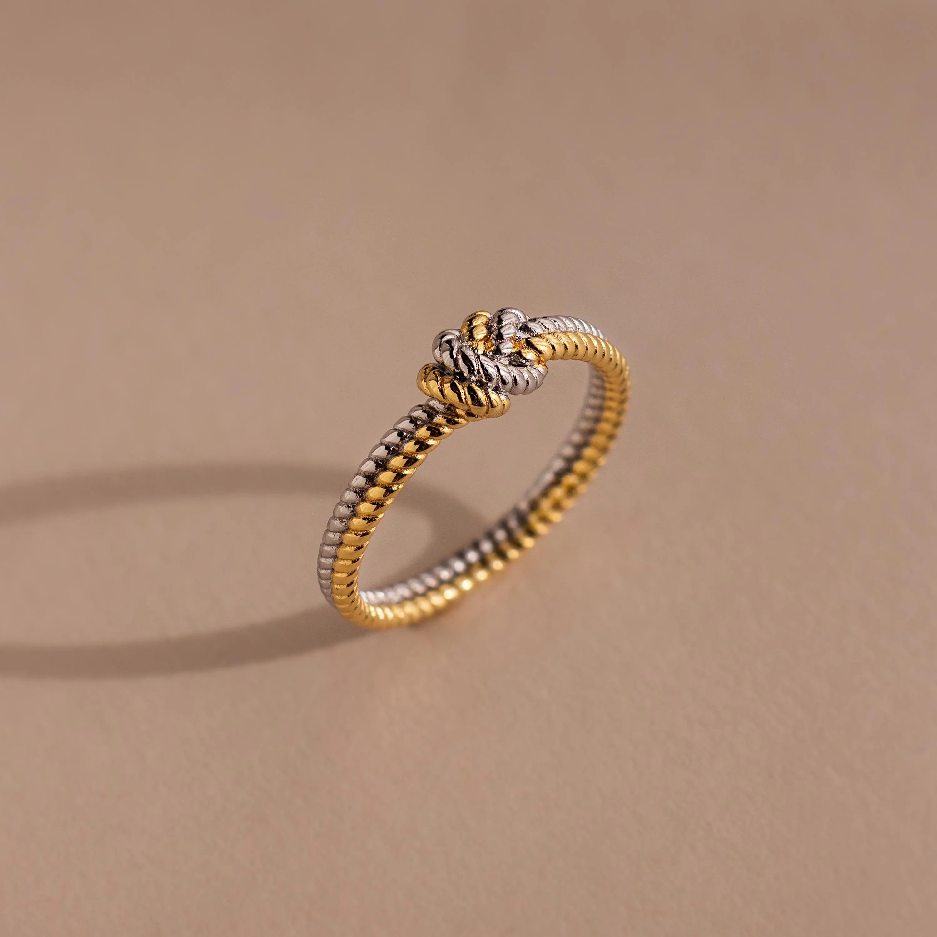 The Mixed Metal Knot Ring features a gold and silver twisted rope design with a knot, making it an ideal relationship gift. Shown on a beige background.