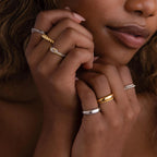 A woman's hands showcase the Mixed Metal Knot Ring—crafted in gold and silver—and other bands, held near her face in soft lighting, making it a perfect relationship gift.