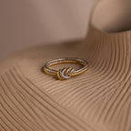 The Mixed Metal Knot Ring, ideal as a relationship gift, features gold and silver twists and rests elegantly on a textured beige surface.