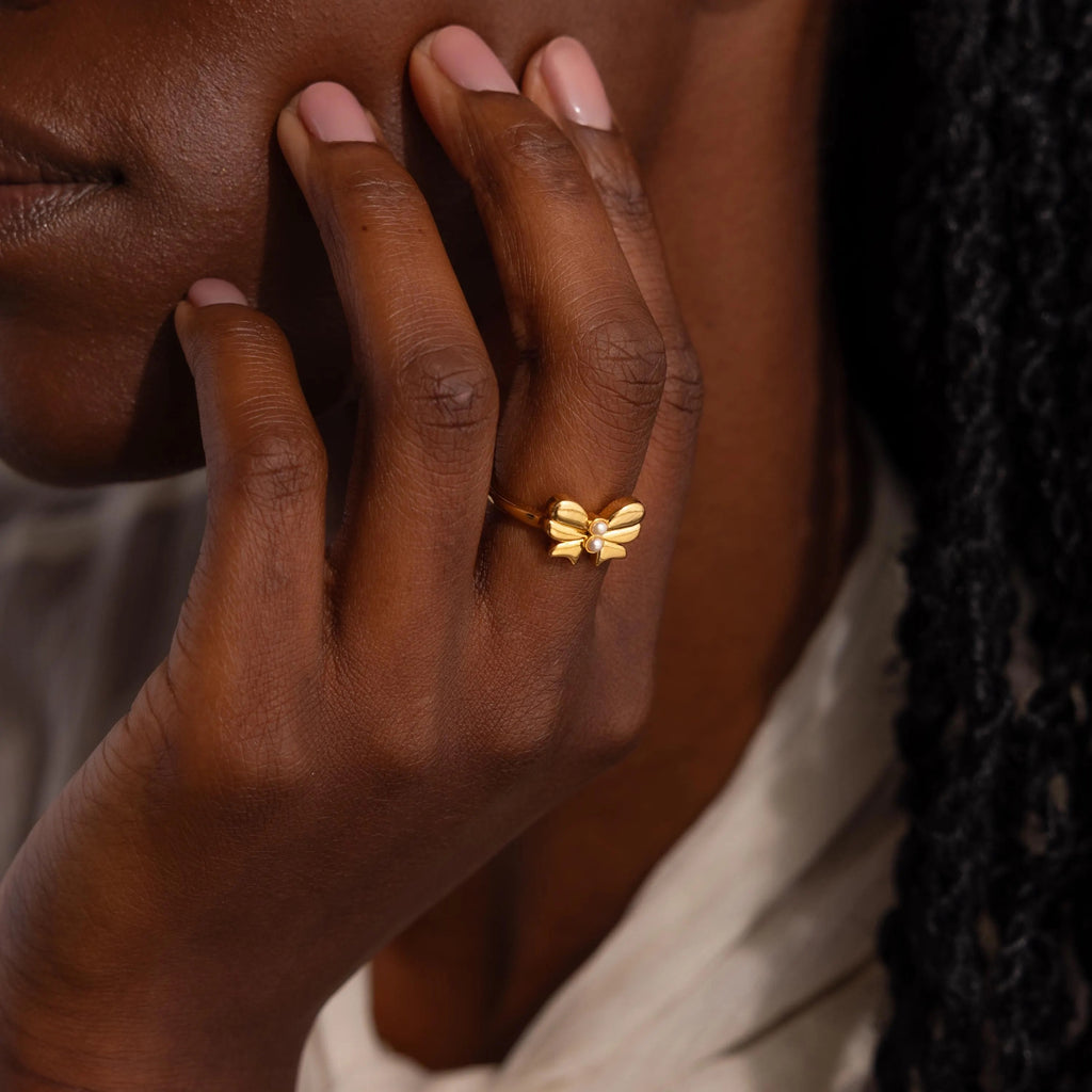 A woman wears the gold Bow Pearl Ring on her finger, showing how it looks when styled on the hand.