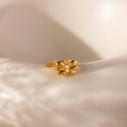 The gold Bow Pearl Ring is displayed on a softly lit, curved cream surface, highlighting its delicate design.