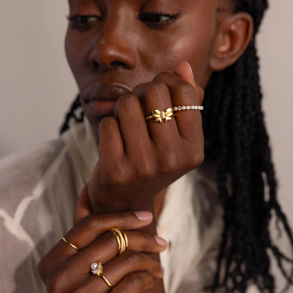 A model wears the Bow Pearl Ring paired with other gold rings, showcasing a layered, chic jewelry styling.